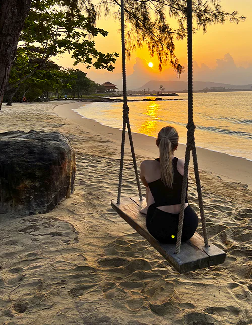 En person sitter på en huske på en strand og nyter solnedgangen