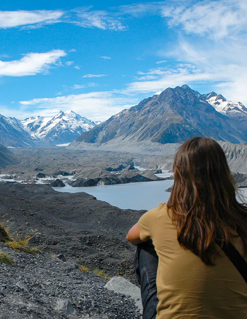 Person som beundrer de snødekte fjellene og den vakre breinnsjøen i Aoraki/Mount Cook nasjonalpark, New Zealand