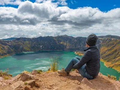 En kvinne sitter på kanten av kratersjøen Quilotoa i Ecuador.