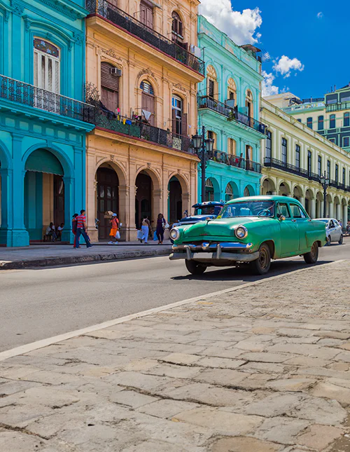 Fargerike koloniale bygninger på Cuba og en klassisk grønn bil i en solfylt bygate.